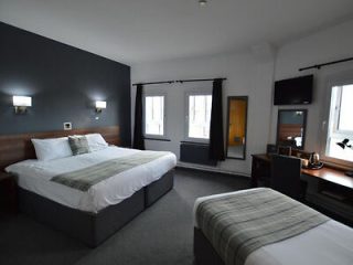 Spacious hotel room with a modern aesthetic, displaying a large bed with striped bedding, additional single bed, and a practical work desk near a window.